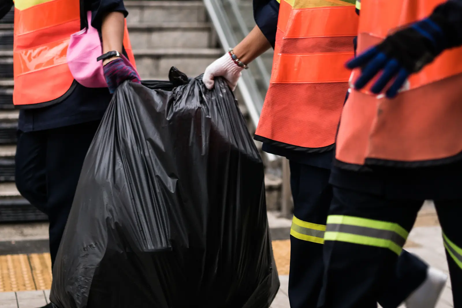 Crew in orange safety vests carrying a full black trash bag